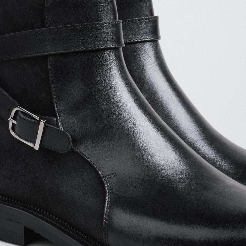 Close-up of black leather boots with buckles on a light gray background