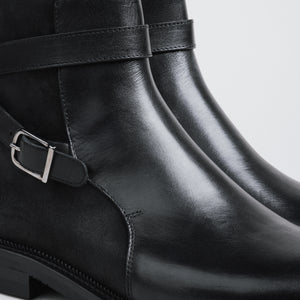 Close-up of black leather boots with buckles on a light gray background