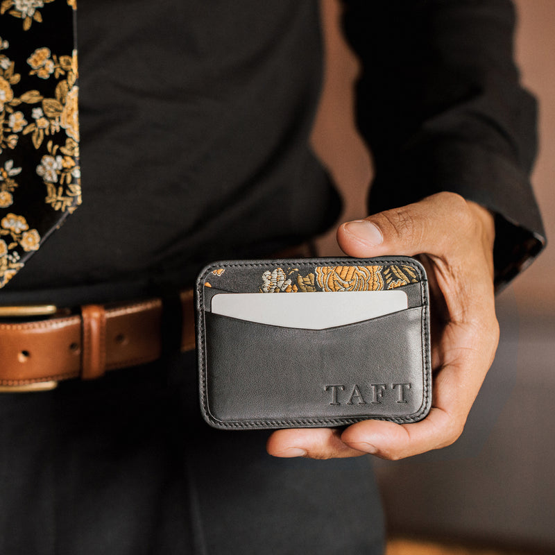 Person holding a gray cardholder with floral design on the back, branded 'TAFT'. - lifestyle